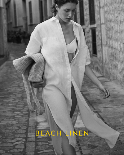 Woman in a white Getaway Shirt Dress walking outdoors with 'Beach Linen' text.