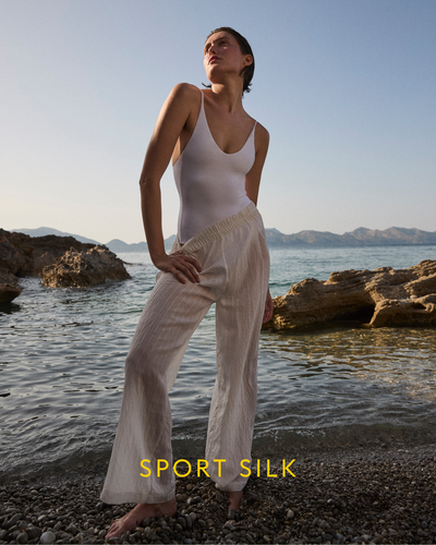 Person wearing a white Sunday Suit and Day Trip Pant Sheer Stripe by a body of water with 'Sport Silk' branding.