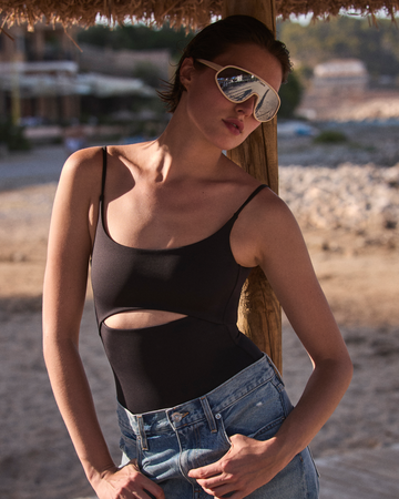 Woman wearing a black Peak Suit and blue jeans with sunglasses on a beach.