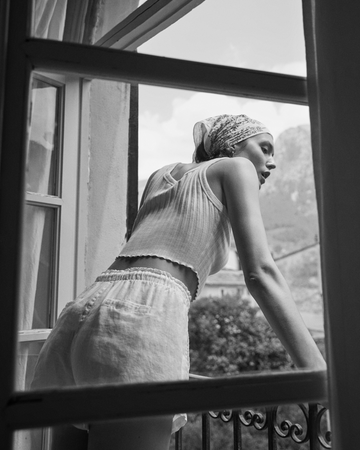Person wearing a white sleeveless top and Getaway Short, standing by a window with a scenic view.