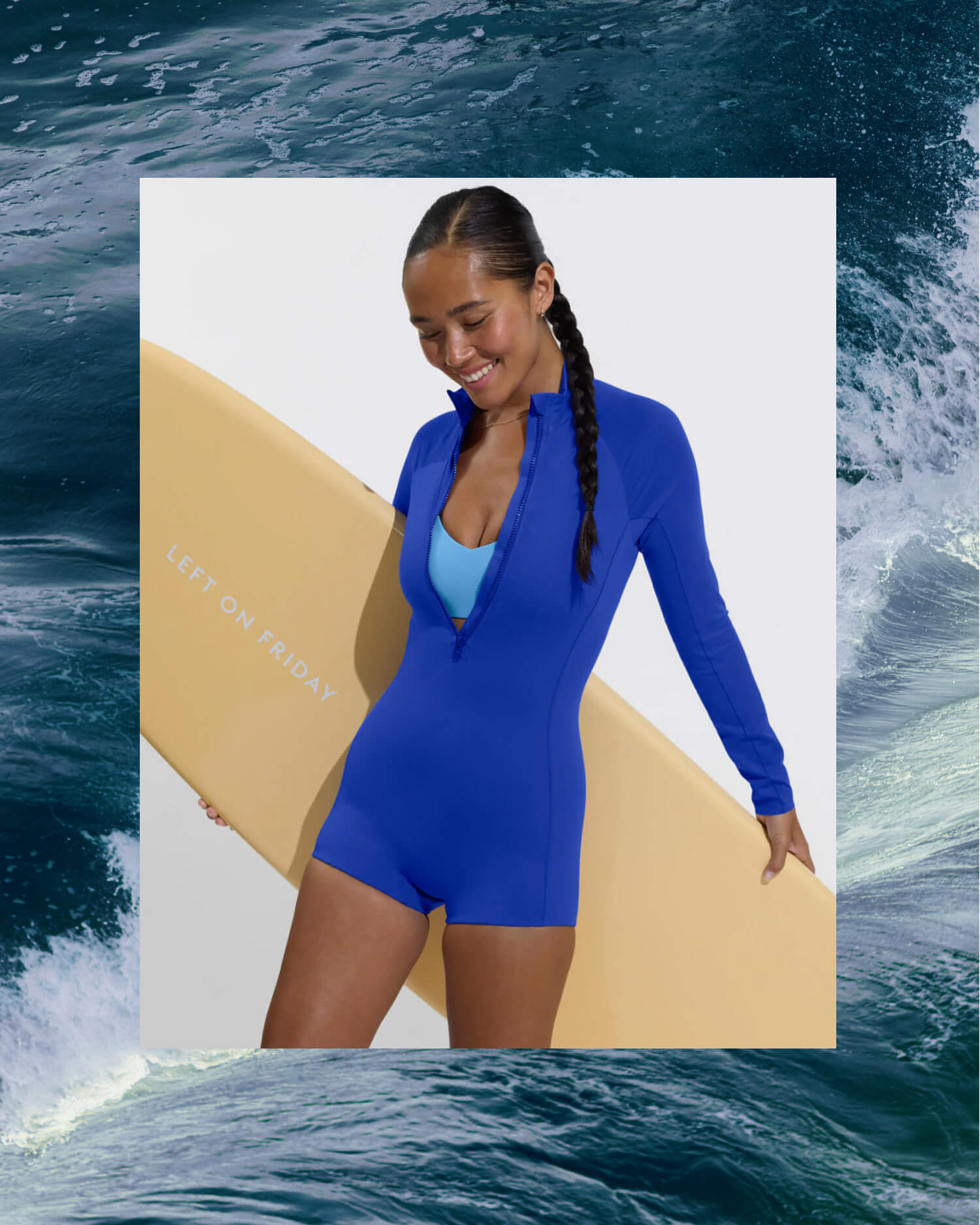 A woman modeling the Rays Suit Shortie in First Place with a front zipper, standing on a white background and holding a yellow surfboard. The surfboard has the text 'LEFT ON FRIDAY' printed on it.