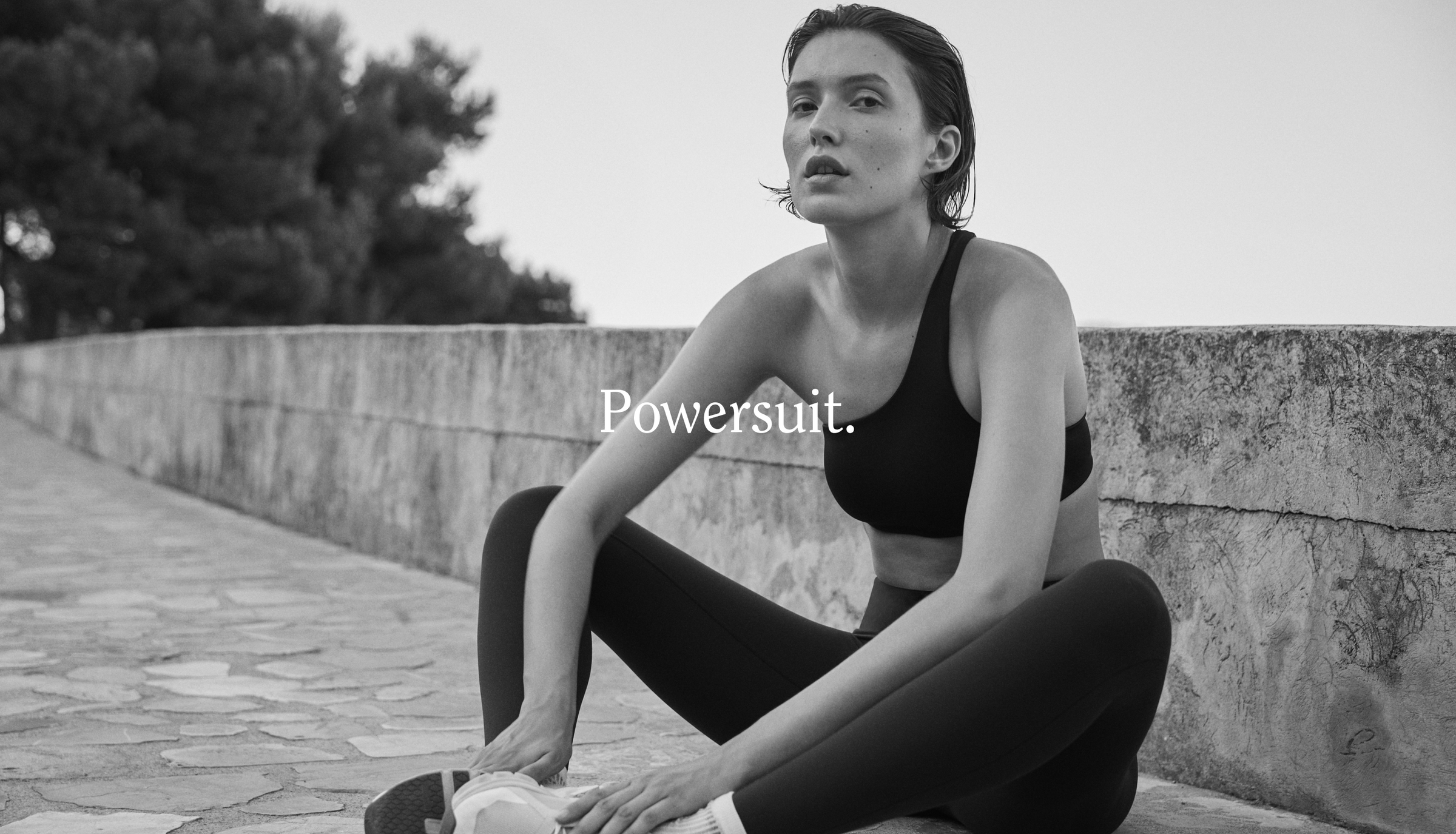 Woman in black Offshore Top + Super Moves Tight sitting on a stone wall with 'Powersuit' text overlay.