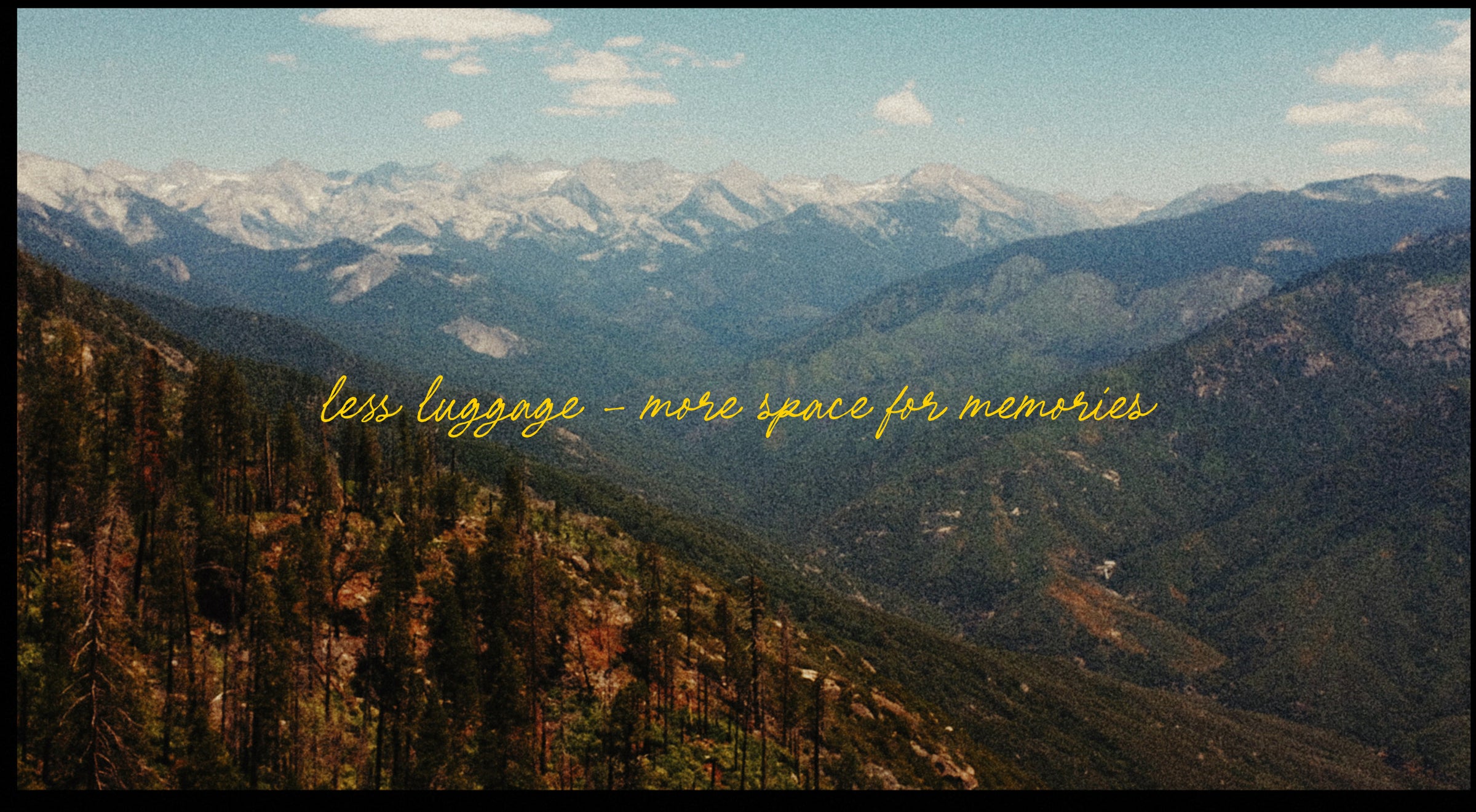 A scenic mountain landscape with snow-capped peaks in the distance, forested slopes in the foreground, and yellow handwritten text across the center reading 'less luggage - more space for memories'.