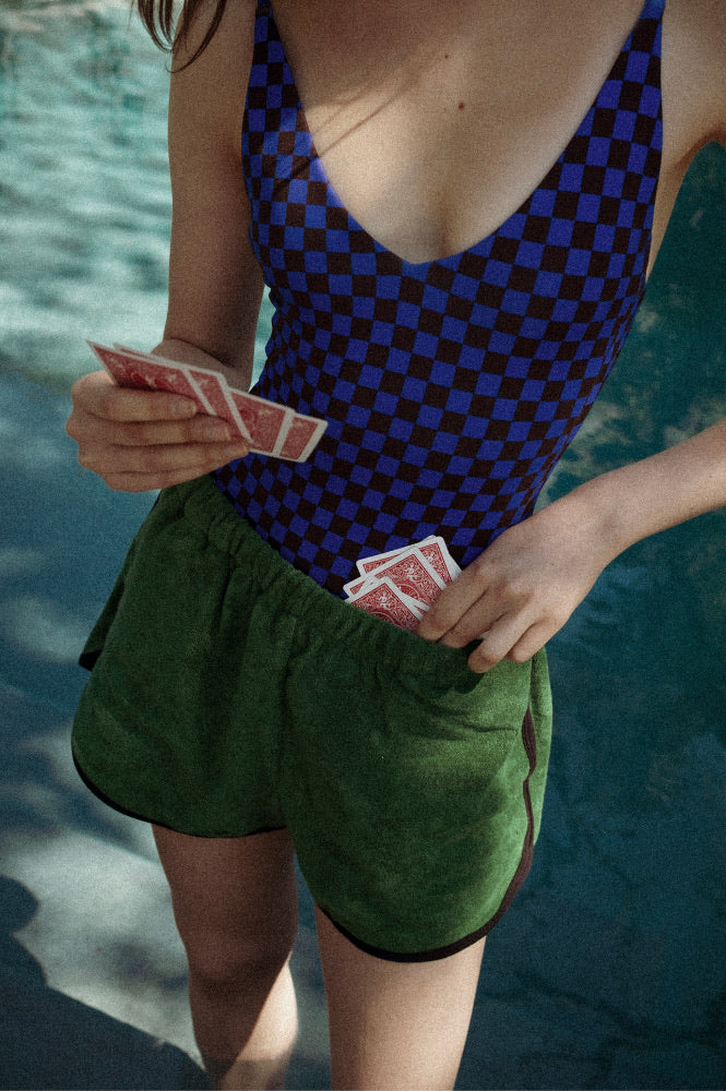 Person wearing a blue and brown checkered Sunday Suit with green shorts, holding playing cards by a pool.