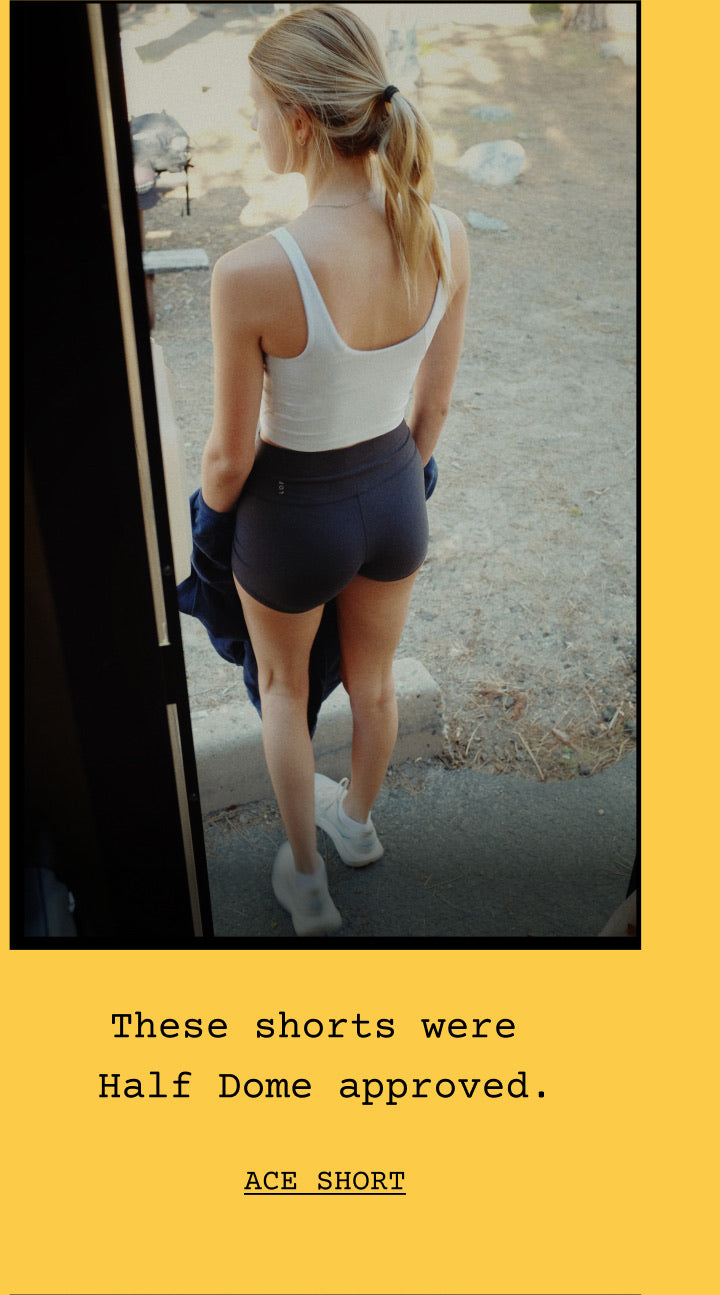 A woman wearing replay tank in coconut paired with ace short in jet. The photo is framed with a yellow border and text below reading, 'These shorts were Half Dome approved.