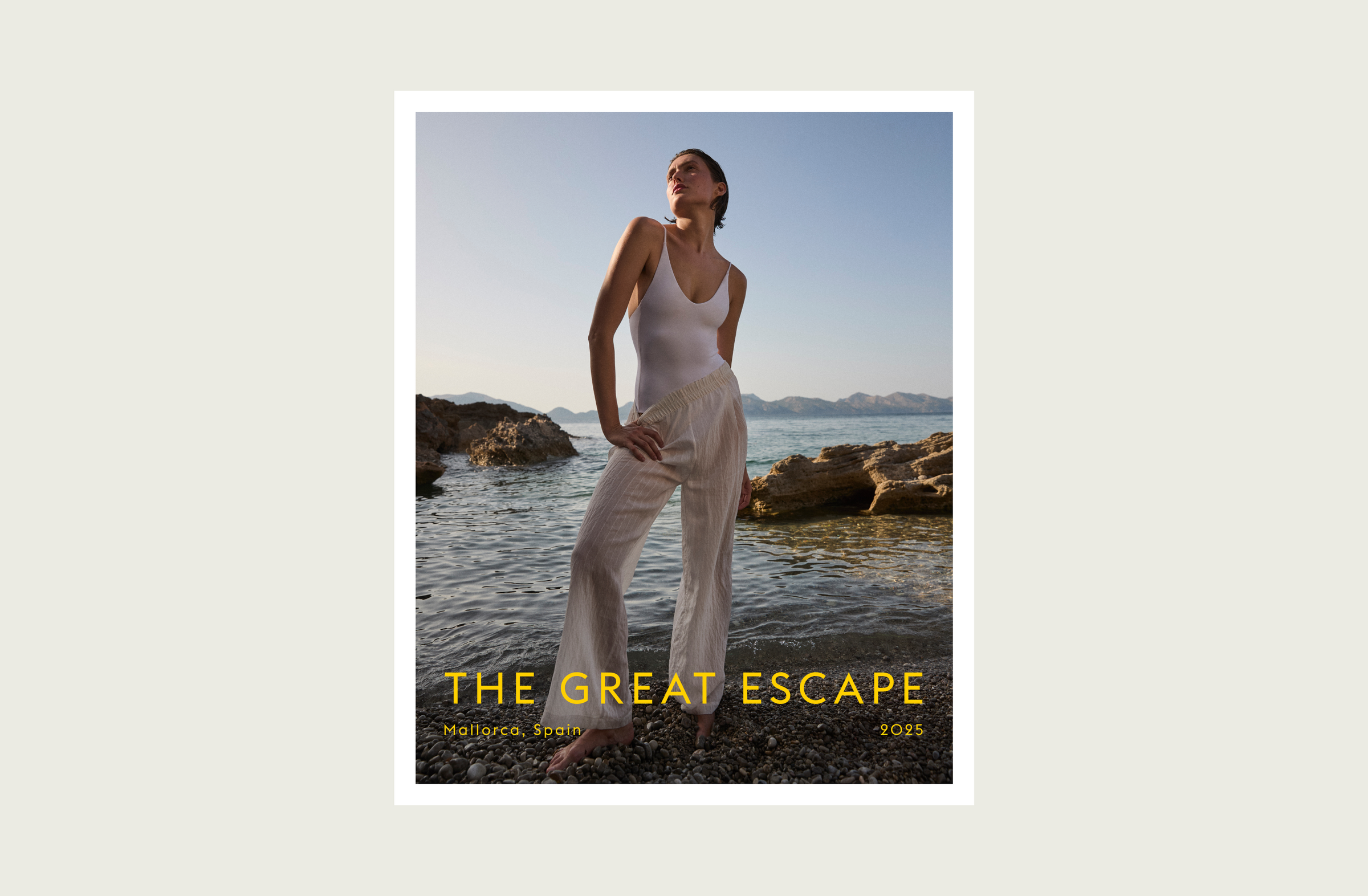 Woman in a white Sunday Suit and Day Trip Pant Sheer Stripe standing by the water with 'The Great Escape' text overlay.